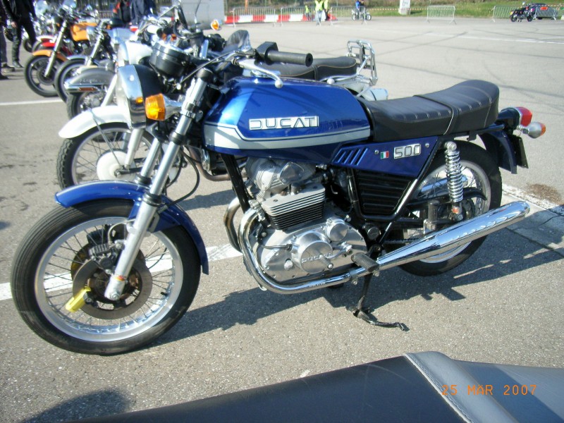 Ducati 500 twin
Eine Ducati paralel twin auf dem besucher parkplatz.  Diese twins von Ducati waren kein erfolg und sieht man heute kaum noch.
Ducati twin seen on the visitors parkinglot . These twins from Ducati were no succes and you almost  don´t see them anymore.
