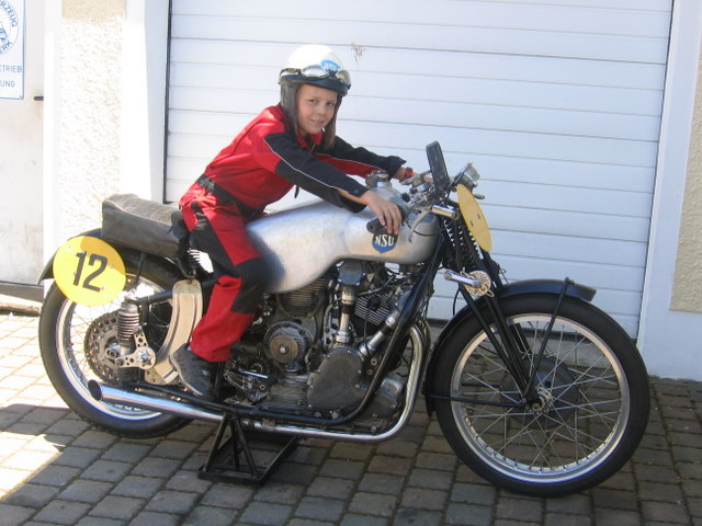  NSU Kompressor  500 ccm  Deutsche Motorradlegende
NSU 500 Kompressor 1949.Bereits im Winter 48/49 stellte NSU die erste deutsche Nachkriegs Werksmanschaft auf. Wilhelm Herz hatte in den Trümmern des NSU Werkes zwei der 350ccm Vorkriegsmaschinen bergen können,mit denen er 1948 in der 350ccm Klasse Deutscher Meister wurde,und mit einer aufgebohrten 385ccm  Version in der 500er Klasse Erfahrungen sammelte. Er überließ die Maschinen den NSU Werken zurück und erhielt als Gegenzug  einen Werksfahrer Vertrag.Dort wurden für die 600er Gespannklasse und die 500er Soloklasse die sogenannten RK II (Rennkompressor 2. Ausführung mit einem Kurbelhaus welche Platz für eine echte 5ooer Welle aufweist) aufgebaut die in der Endphase 98PS leisteten.Anfang der Saison 1949 traten Probleme mit einem neuen 10 Flügel Lader auf ,sodas man den von Herz weiterentwickelten 4 Zellen Lader mit Ausgleichskammer wieder zurückbaute.1950 wurden Böhm/Fuchs Deutscher Gespannmeister,Fleischmann hinter Georg Meier 2. in der Wertung mit einem 50kg Übergewichts Handikap(gemeint ist das Motorrad,aber Fleischmann brachte auch 2 Zentner auf die Waage) Trotz einer Sturzverletzung behielt Fleischmann den Anschluß und die 500er NSU war das schnellste Solomotorrad Weltweit.Bei Testfahreten auf einer Autobahn nahe Neckarsulm wurde festgestellt das die lang übersetzte unverkleidete Strassenrennmaschine 270 km/h erreichte.Weil Aufladung International verboten war, nutzte das aber nur wenigen jedoch sind die Zweikämpfe von BMW und NSU vor hundert Tausenden Zuschauern in die Geschichte eingegengen. Die 350er Klasse konnte Fleischmann aber mit der Vorkriegs Kompressor gewinnen.
1951 und 1956 erreichte NSU mit diesen Motoren den abgsoluten Geschwindigkeits Weltrekord zuletzt 339km/h,bei gestiegener Motorleistung von 110PS.Der letzte offizielle Einsatz des abgebildeten Motors war im Spätjahr 1966 als Wilhelm Herz in Ramstein den Weltrekord  von 10km mit 304 km/h holte.
