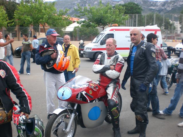 Bultaco TSS 350
Auf der Maschine Ginger Molloy, der junge Mann mit den Helmen Gingers Mechaniker Garry, rechts neben der Maschine, der Eigentümer Vicente Ballester, der sie freundlicherweise Ginger zur Verfügung gestellt hat. Der "gelangweilte" Blick von Ginger täuscht, wir hatten eine Menge Spass zusammen. Besonders am Freitag. Die Geschichten, die diese "alten Haudegen" draufhaben sind einfach unschlagbar.

