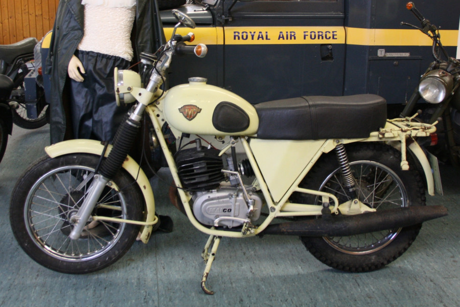 1976 M250/M Military
Die Maico M250/M „Military“ wurde von Juni 1976 bis Juli 1978 in etwa 330 Exemplaren gebaut. Die Maschine wurde in den frühen 1970er Jahren für eine Ausschreibung der Bundeswehr entwickelt. Die Bundeswehr entschied sich aber aus wirtschaftlichen Gründen für die Weiterverwendung ihrer Hercules K125.
Maico gelang es schließlich 250 Maschinen des Typs M250/M an die Armee des Sudan zu verkaufen. Weitere 80 Maschinen wurden auf dem deutschen Markt verkauft. Der 30PS Geländesportmotor wurde allein über einen 26er Bing-Seitenschwimmervergaser und den Auspuff auf versicherungsgünstige 17PS gedrosselt. 
Wegen des schleppenden Absatzes des häßlichen und schlecht abgestimmten Motorrades wurde die Military Maico-Händlern und Fahrschulen mit einem beigepackten 32er Vergaser zu Sonderkonditionen offeriert. Die gezeigte Maschine wurde Ende Oktober 1976 gebaut und an den Maicohändler Werber in Bad Krozingen ausgeliefert.

